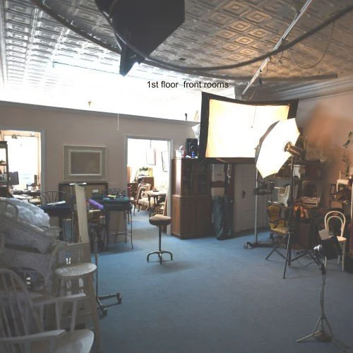 A photography studio with lighting equipment, a high stool, and furniture in the background