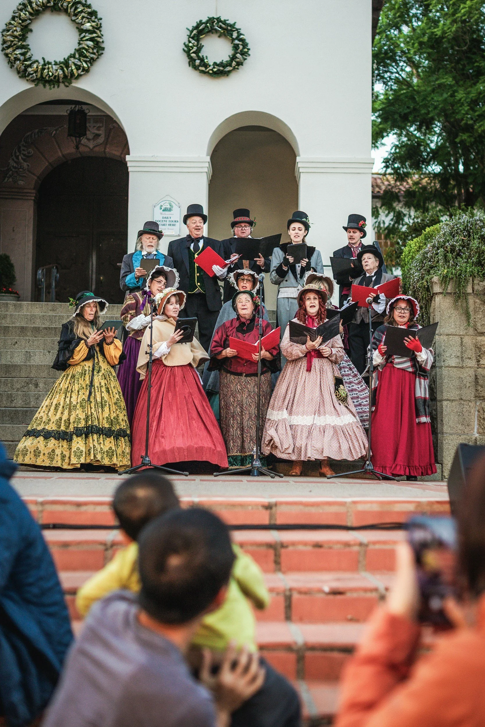 A group of people dressed in vintage 19th-century clothing performing in a choir outdoors
