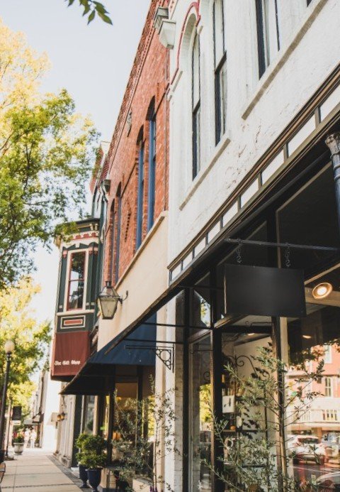 Street view of historic brick storefronts with black awnings under a blue sky