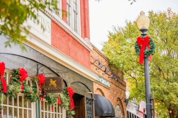 Historic brick storefronts decorated with festive holiday wreaths and red bows