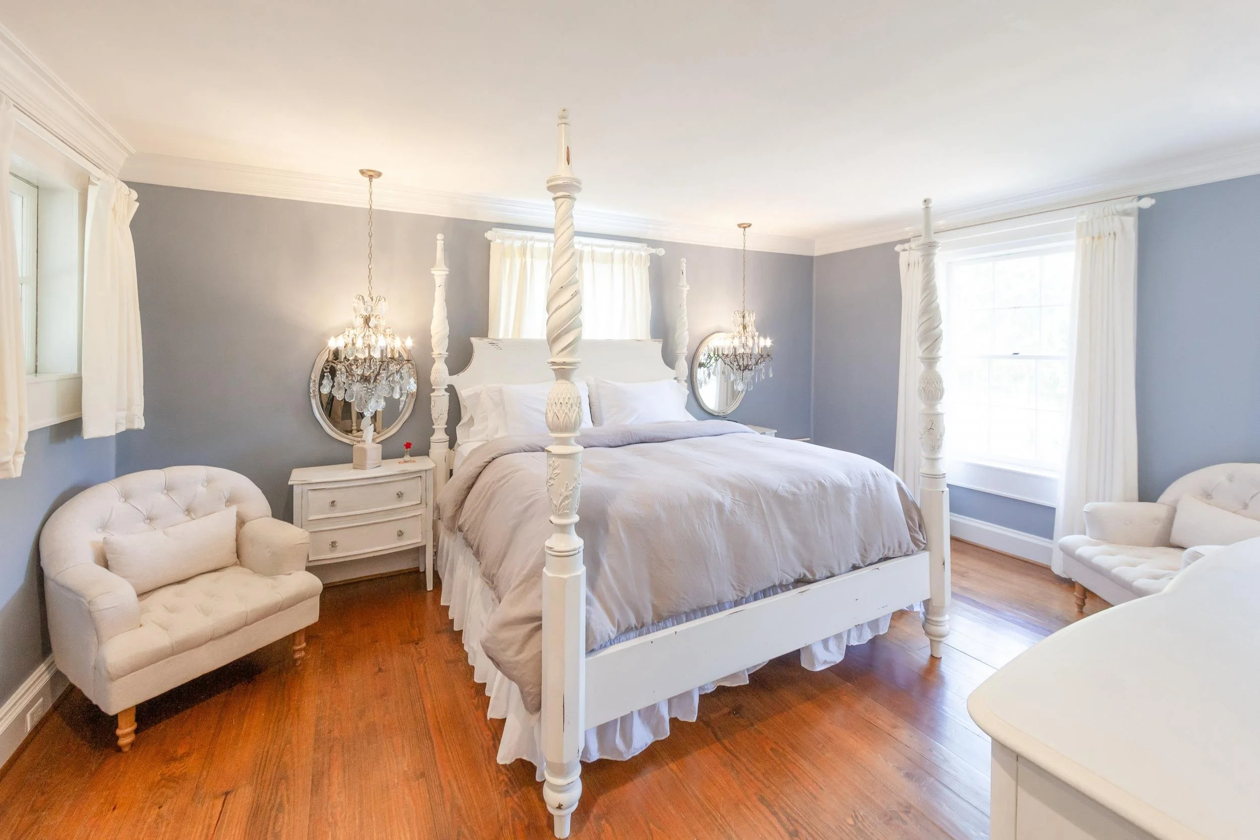 A bedroom with a white canopy bed, white furniture, and light blue walls