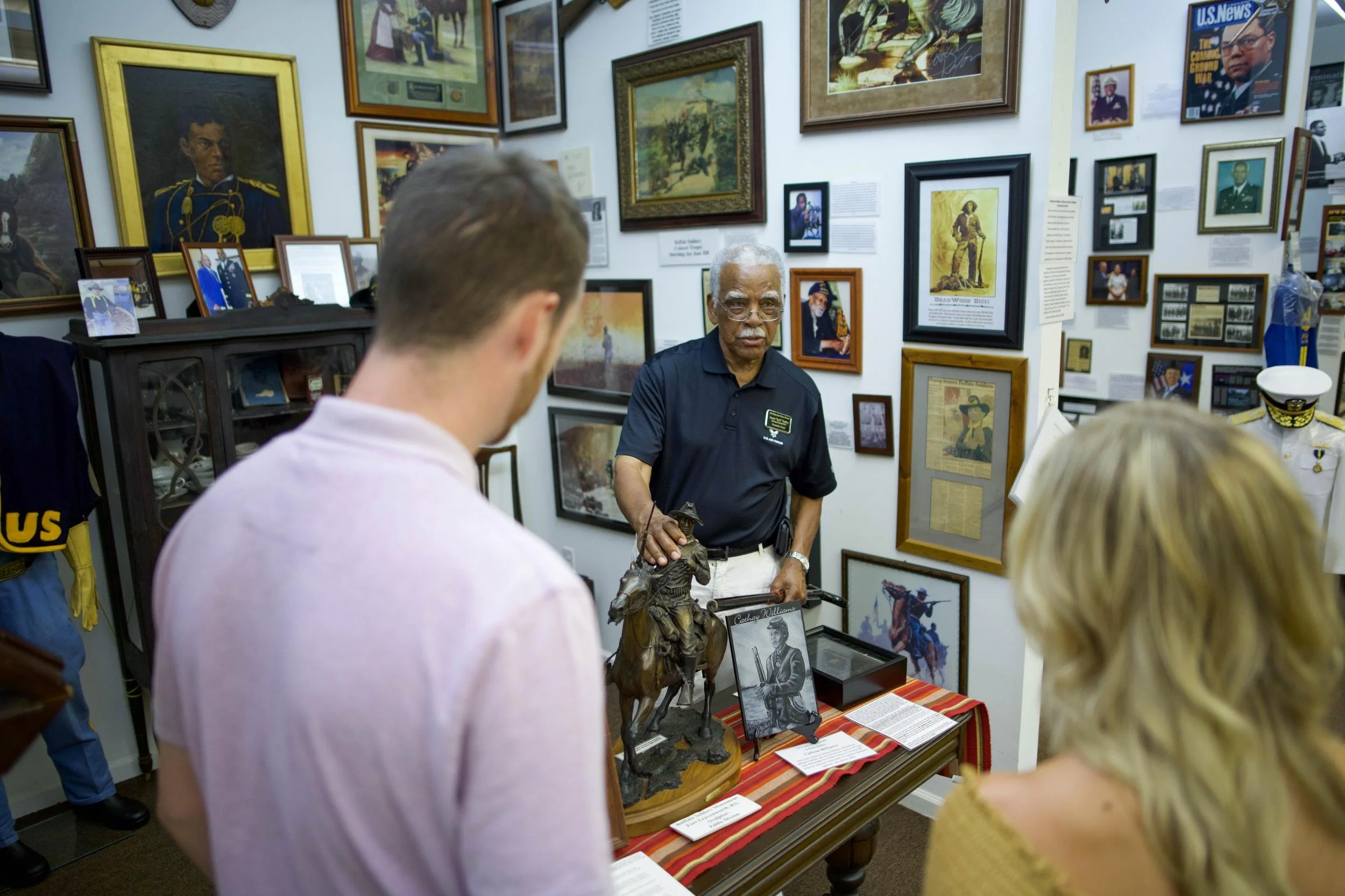 Visitors watch a guide holding a sculpture in a museum filled with paintings