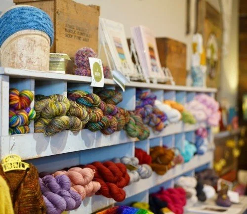 Display of colorful yarn and knitting supplies on store shelves.