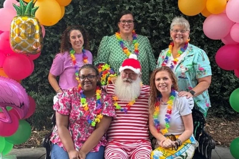 A group of people dressed in colorful Hawaiian shirts celebrating a Christmas in July event
