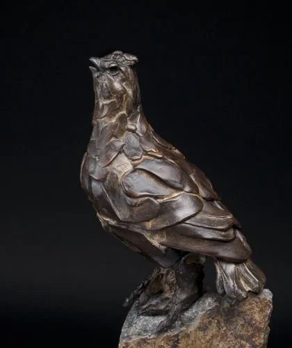 Bronze sculpture of a quail mounted on a rock against a black background