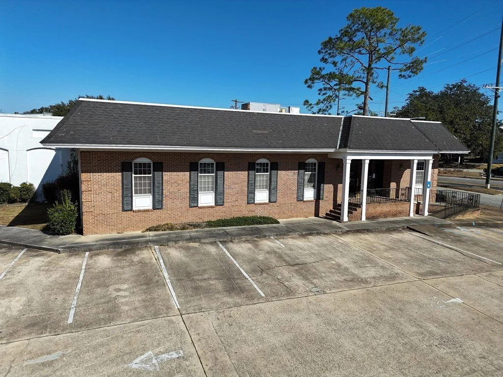 A single-story brick commercial building features a dark roof and white-pillared entrance