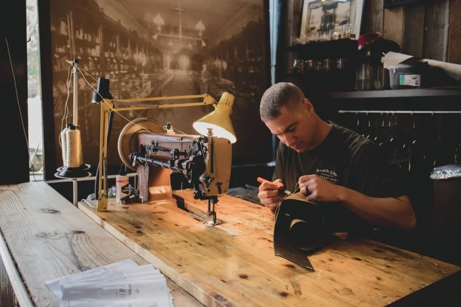 a craftsman working on a leather project at a wooden counter, using a vintage-style sewing machine