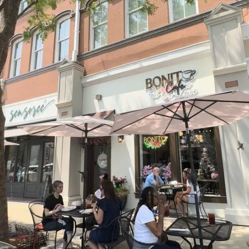People sitting outside at tables under umbrellas in front of a cafe with a "Bonito" sign