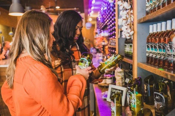 two people browsing through a display of wine bottles at a warmly lit store