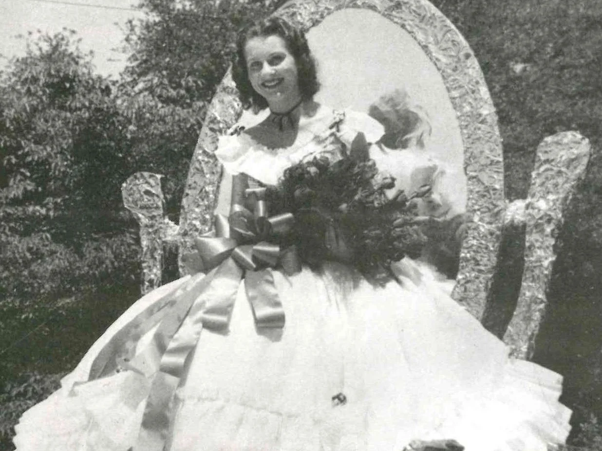 A black and white photo of a woman wearing a white dress holding roses