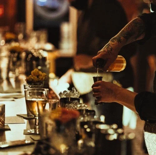 Close-up of a bartender pouring a drink into a glass under warm bar lighting