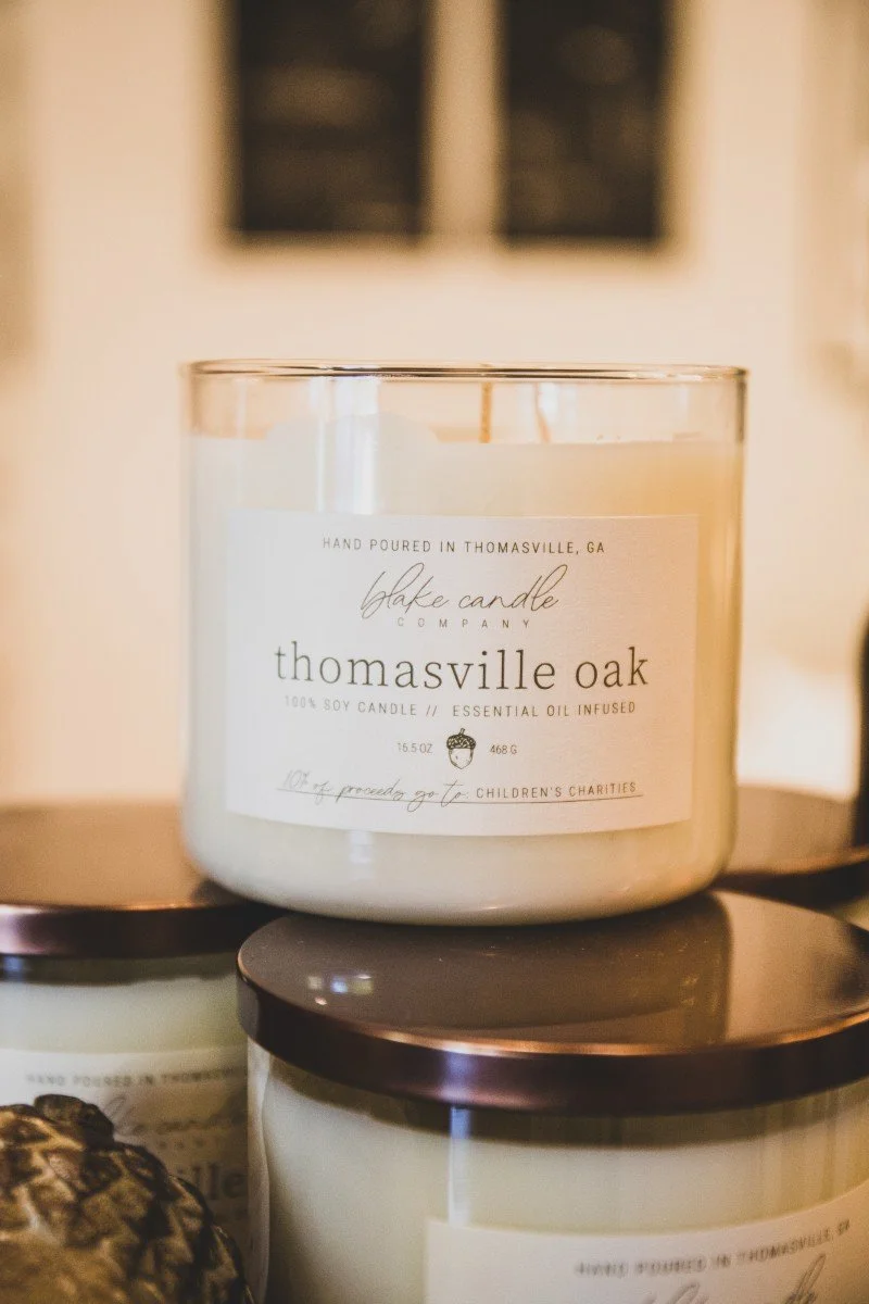 A white candle labeled 'Thomasville Oak,' handmade in Thomasville, GA, infused with essential oil