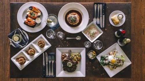 Top-down view of a table with various dishes, including a meat entree, salads, bread, and drinks