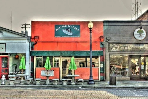 Street view of a building with outdoor seating, tables, umbrellas, and a 'Willard Academy' sign