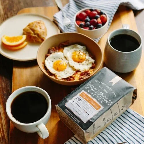 Two cups of coffee, eggs, bacon, berries, and a scone on a wooden breakfast table