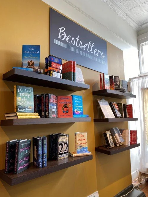 Bookshelves with books and a sign reading 'Bestsellers' on a yellow wall in a bookstore.