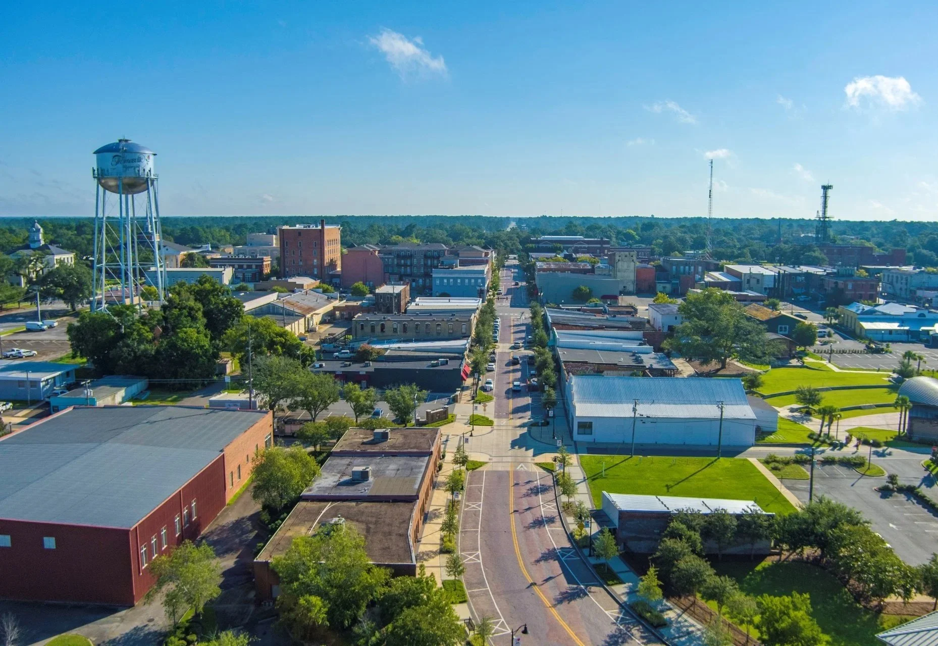 Aerial view of Thomasville with a water tower, streets, trees, and buildings under a clear blue sky