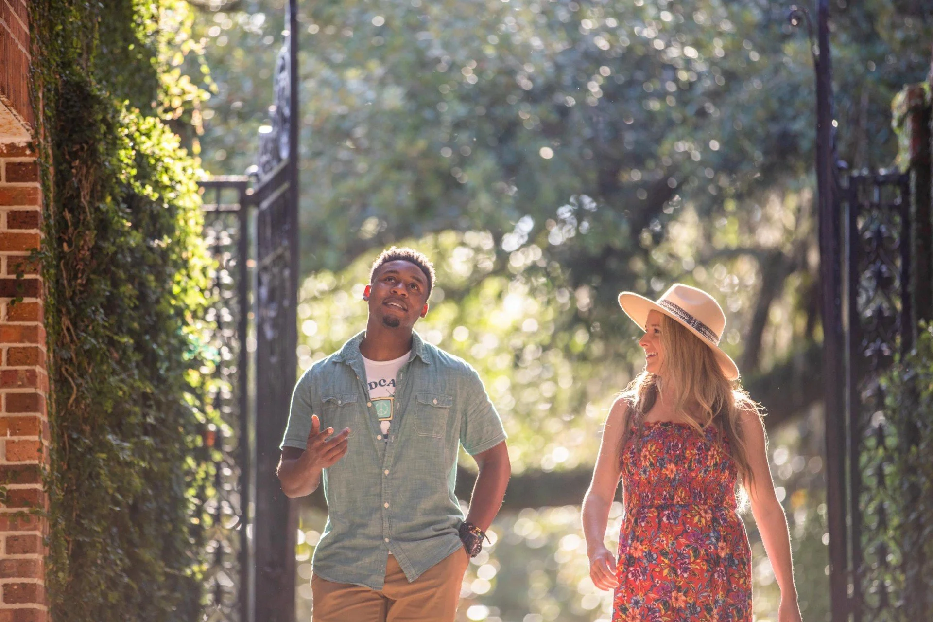 Young man and woman walking outdoors and talking, with sunlight filtering through trees