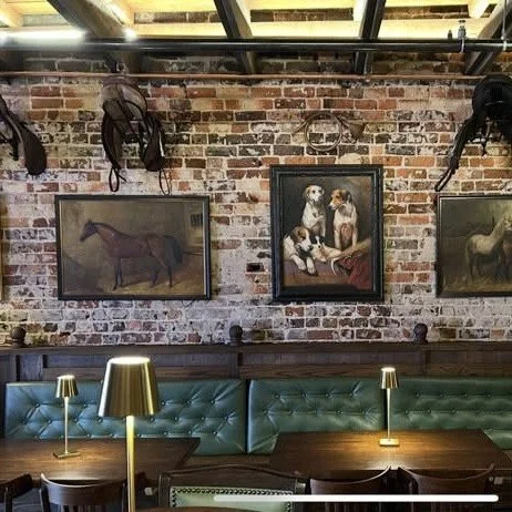 Interior of a restaurant with a brick wall decorated with paintings of horses and dogs