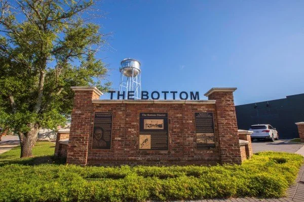 Brick landmark sign reading The Bottom sits in front of a blue sky and water tower