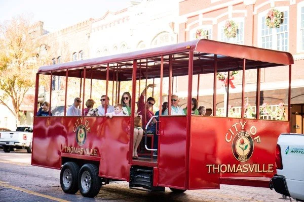 A red City of Thomasville trolley carrying passengers through a festive holiday parade