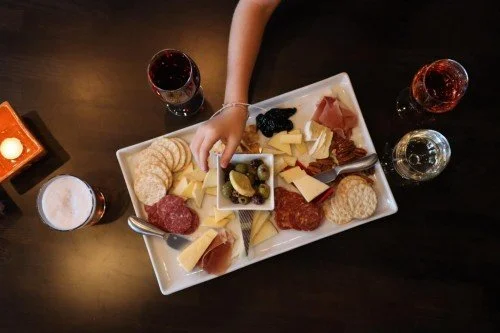 Overhead view of a hand reaching for a charcuterie board with cheeses, crackers, and meats