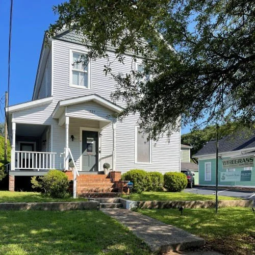 Two-story white house with a covered front porch and a green storefront next door