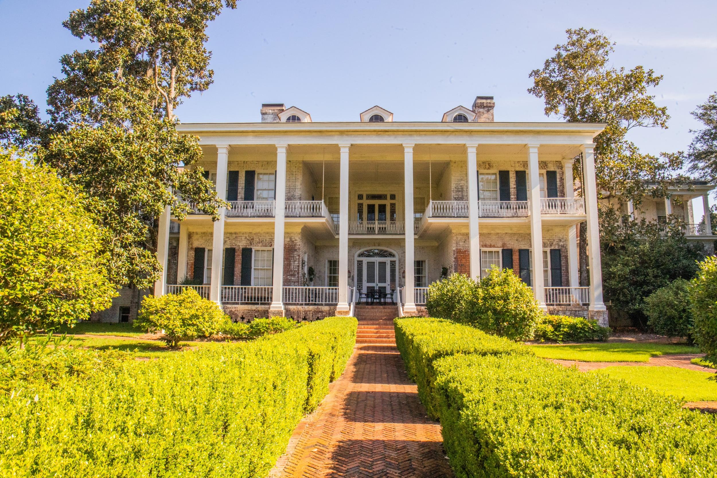A large historic white mansion with a wrap-around porch and massive columns