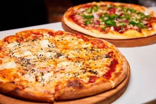 Two pizzas on wooden serving boards: one with cheese, the other with pepperoni and veggies