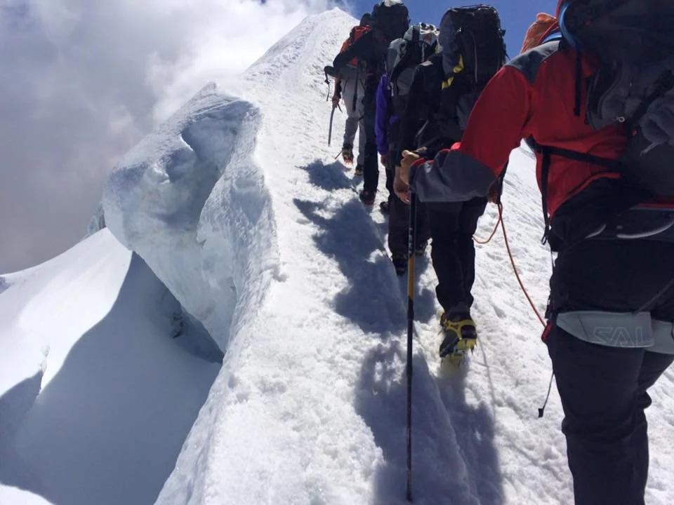 Escursionisti in cordata sulla cresta di una montagna coperta di neve, con un ghiacciaio in vista.