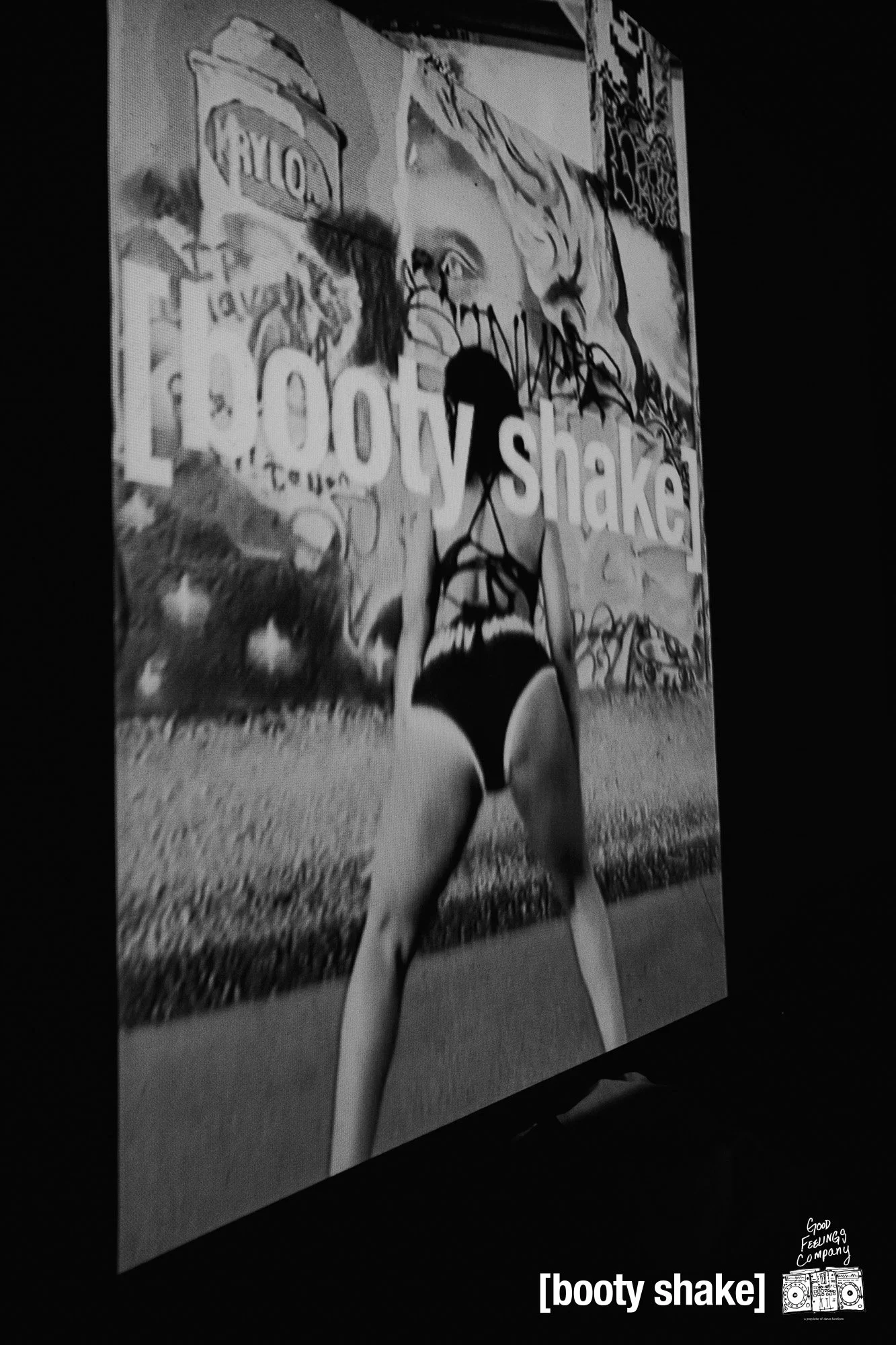A woman in black swimwear standing with her back to the camera in front of a graffiti-covered wall, with the words 'booty shake' overlayed at the bottom and a logo that says 'Good Feeling Company'.