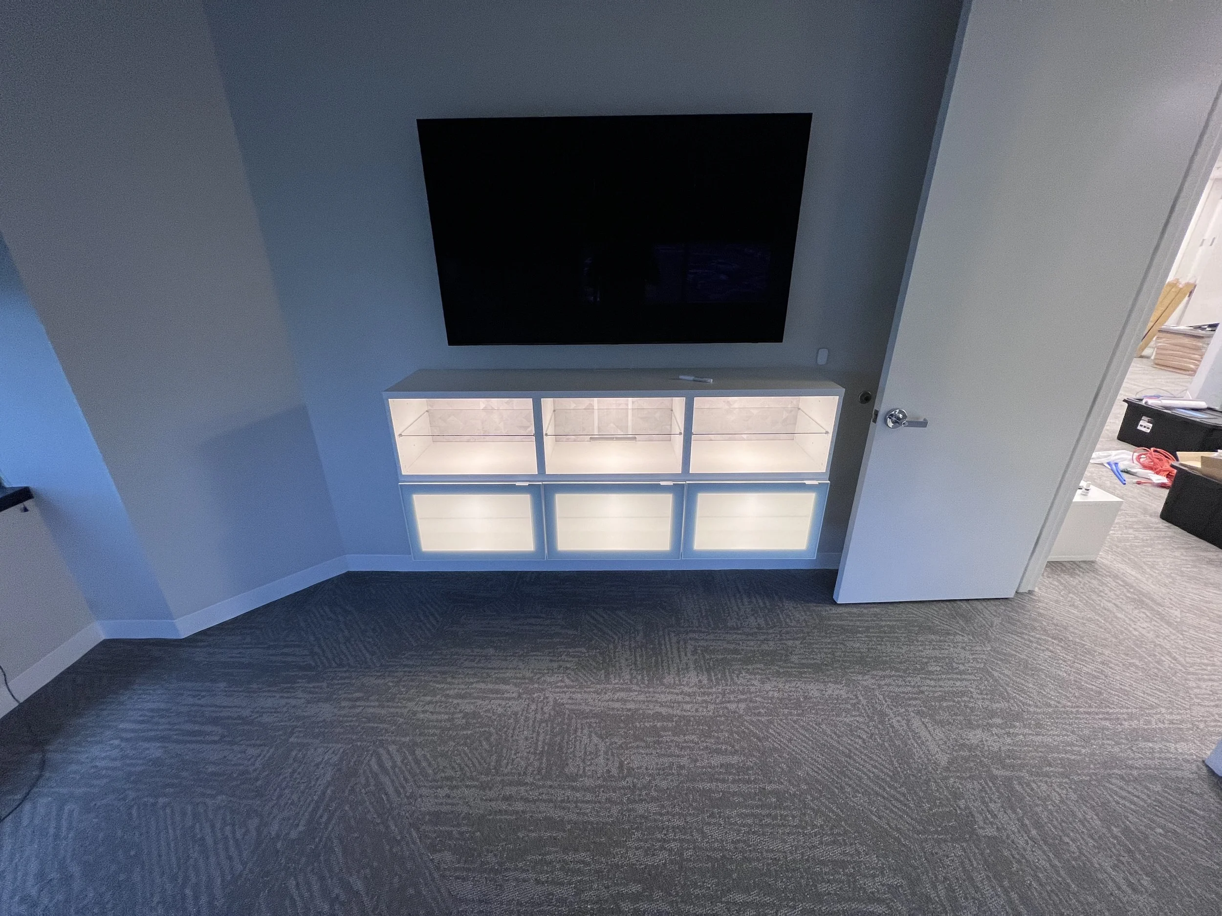 Wall-mounted TV above an assembled TV stand with LED lighting in an office space
