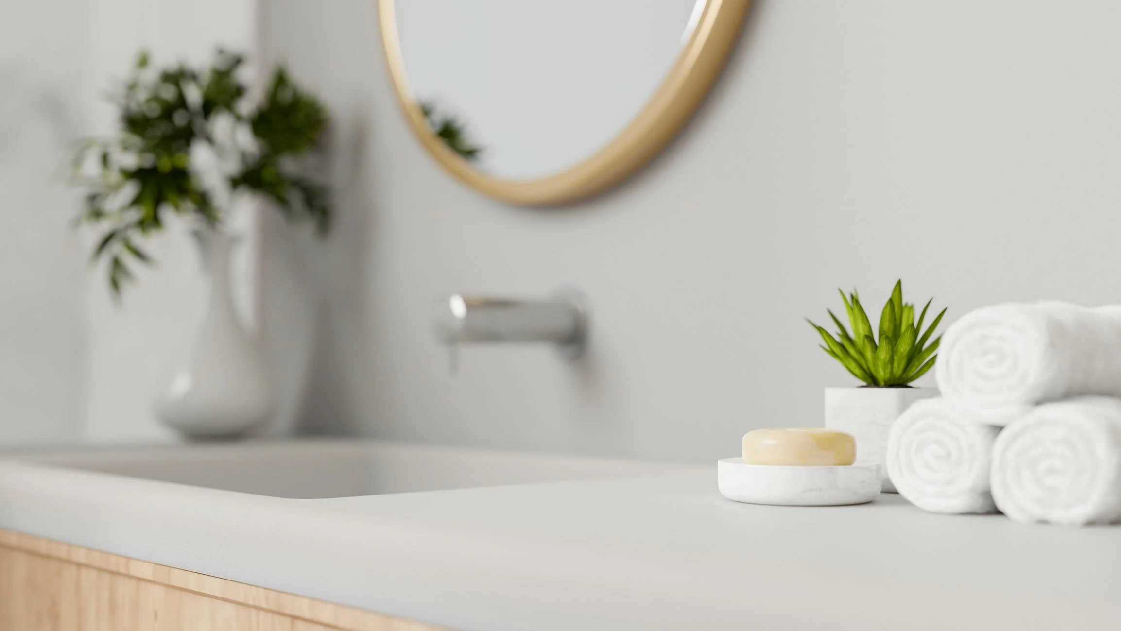 A bathroom counter with rolled white towels, a potted green plant, a bar of soap, and a small vessel, with a mirror and a vase with greenery in the background.
