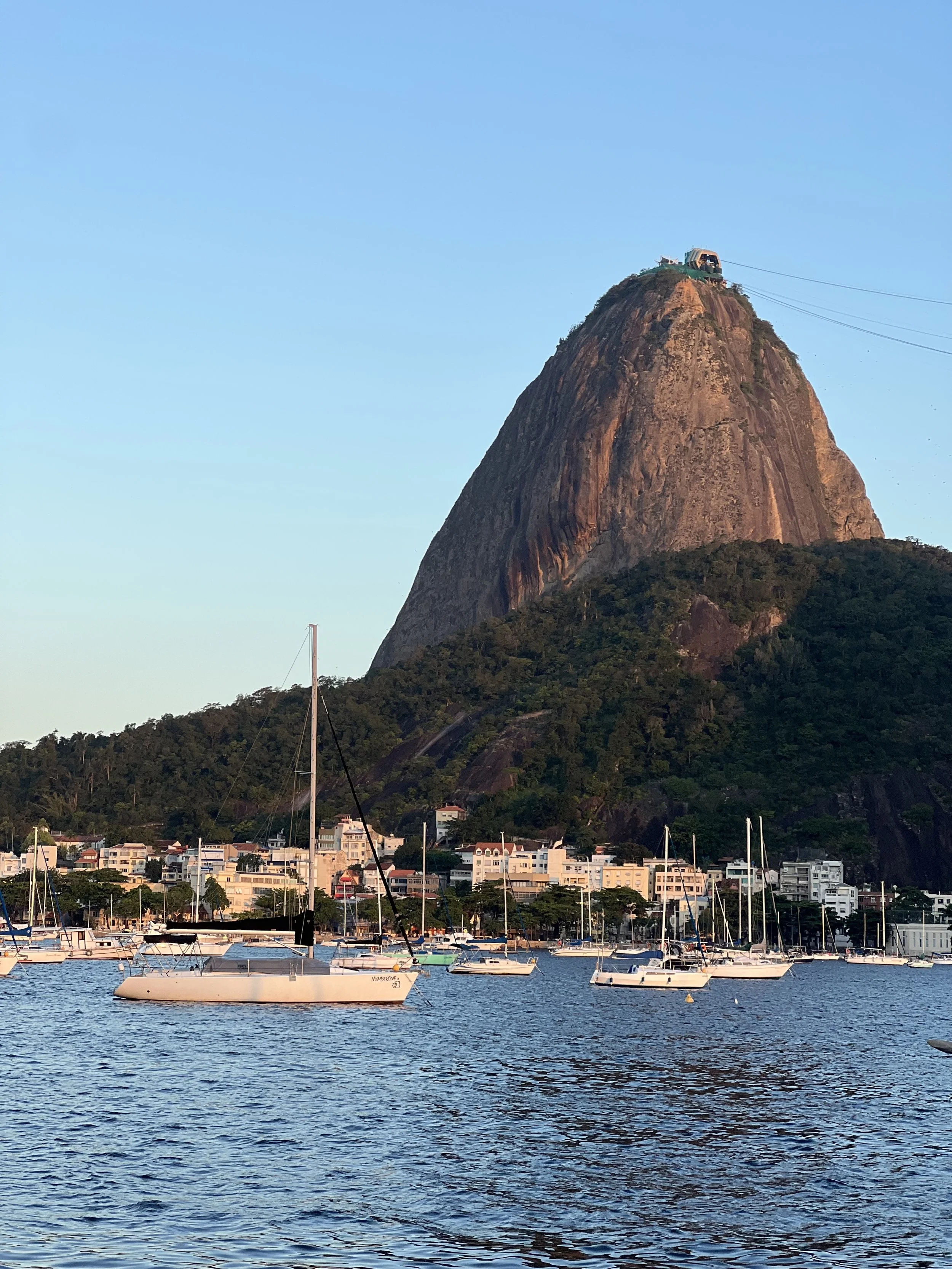 Montanha do Pão de Açúcar ao pôr do sol, com os barcos no mar e edifícios à base.
