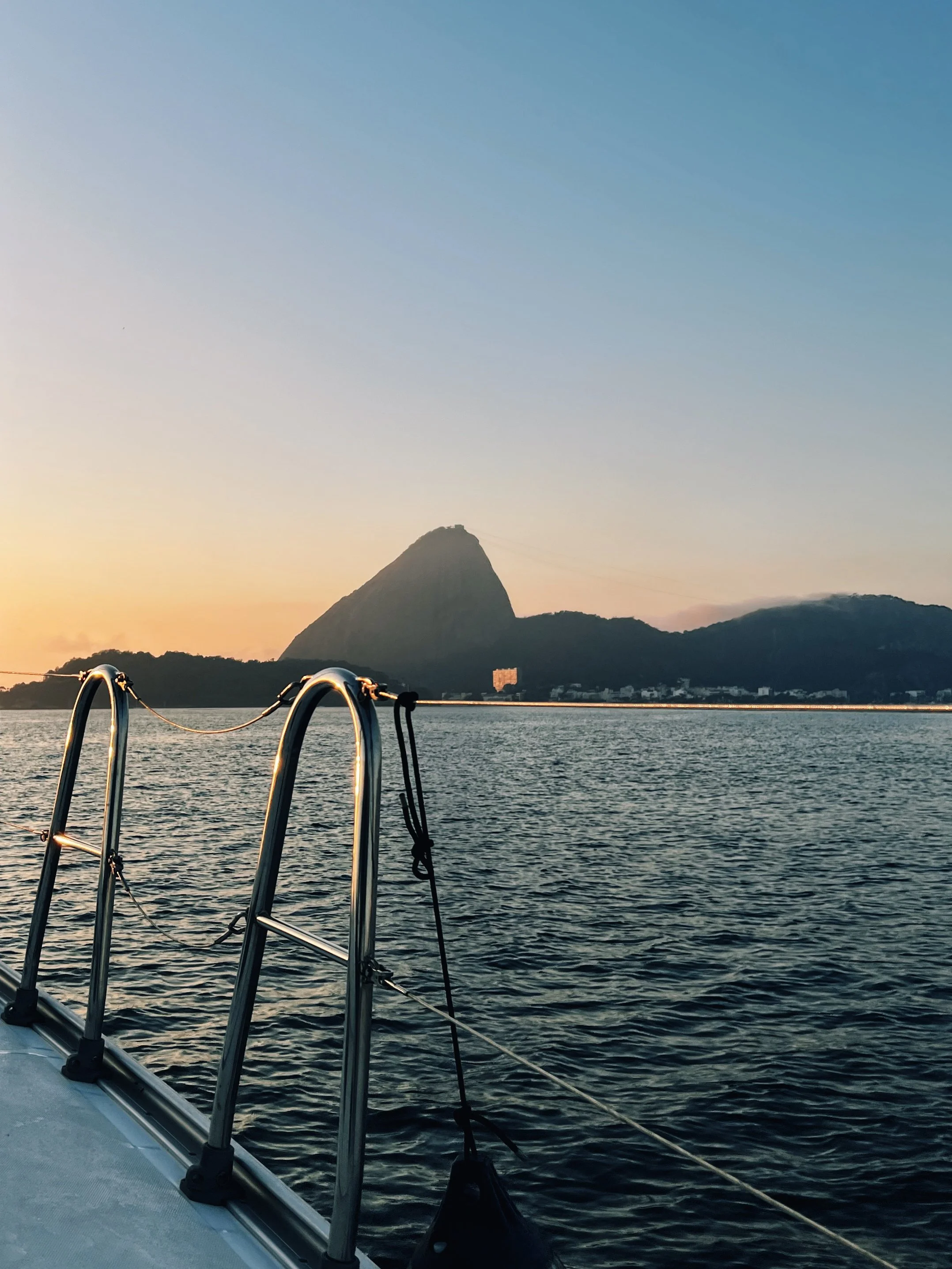 Paisagem com um monte ao fundo, um pôr do sol e um barco com escadas de metal na água.