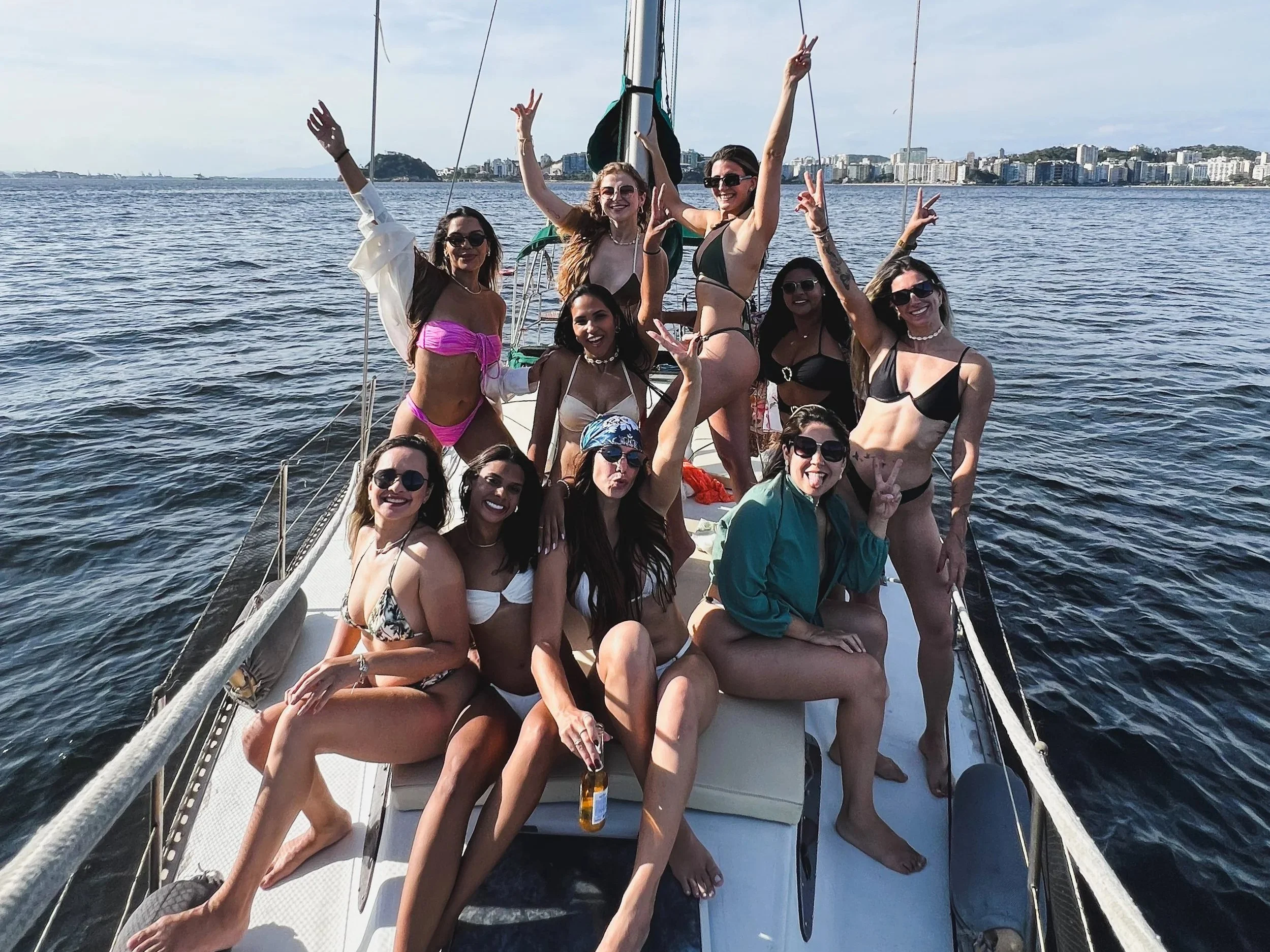 Grupo de mulheres se divertindo em um barco no mar, vestidas com roupas de banho, fazendo poses e sorrindo.