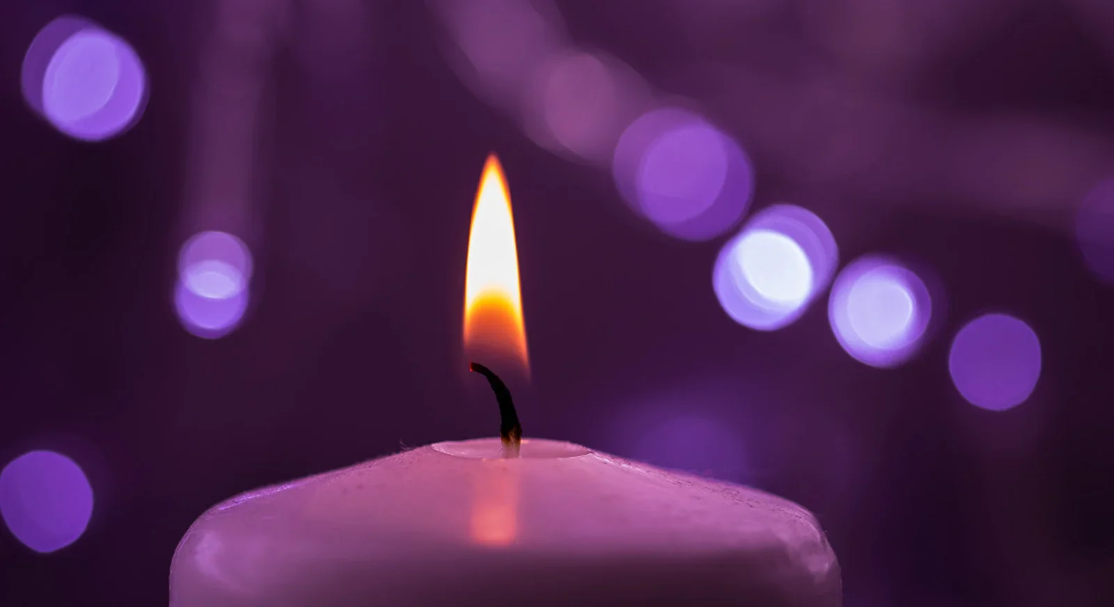 A lit pink candle with a yellow flame against a blurred purple background with circular light bokeh effects.