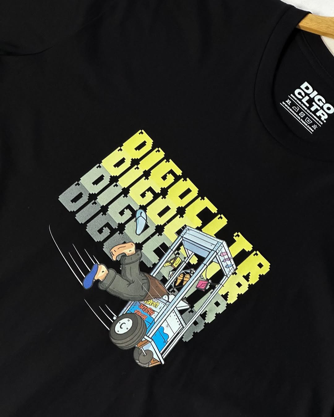 Black T-shirt with graphic design featuring a shopping cart with wheels, a pair of feet in sneakers kicked up, and stacked digital-style block letters spelling 'DIGITAL DISGUST GOOD BAD' in yellow and gray.