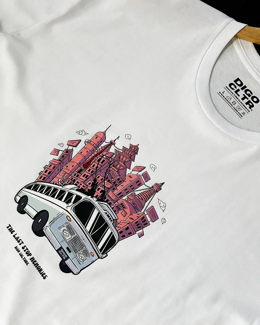 Graphic illustration of a white bus with a cityscape of pink and purple buildings emerging from the top, with small clouds around. Text reads 'The Last Stop Memories' and 'Big Culture'.