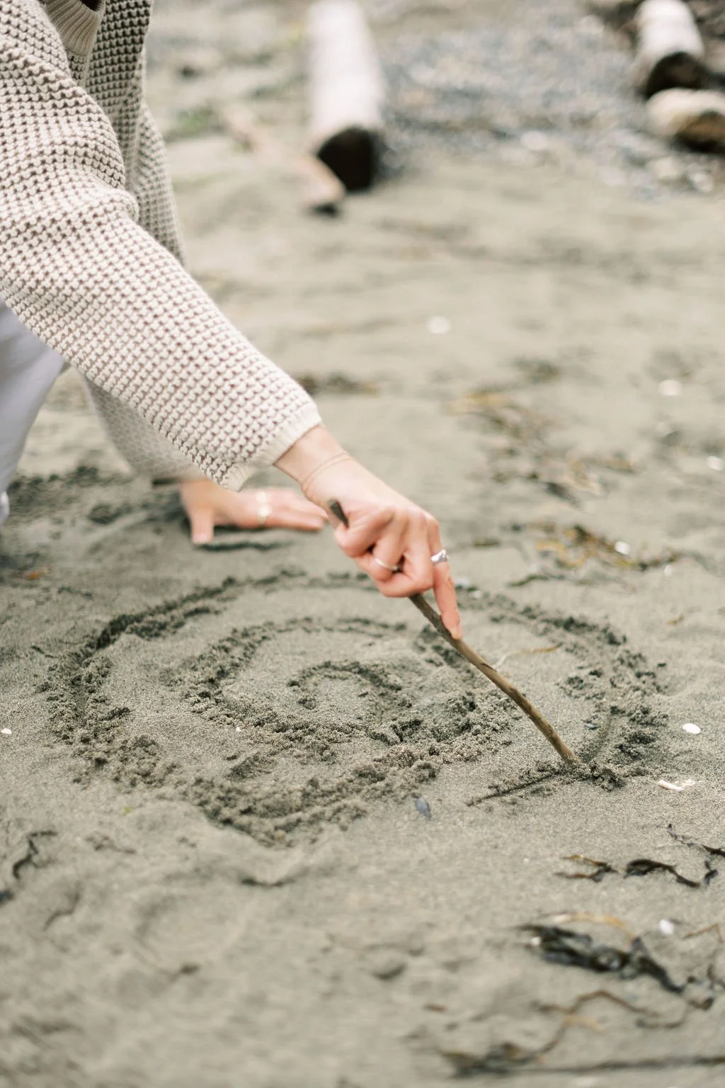 Niki Kairis The Vancouver Death Doula drawing a spiral in the sand with a stick at the beach.