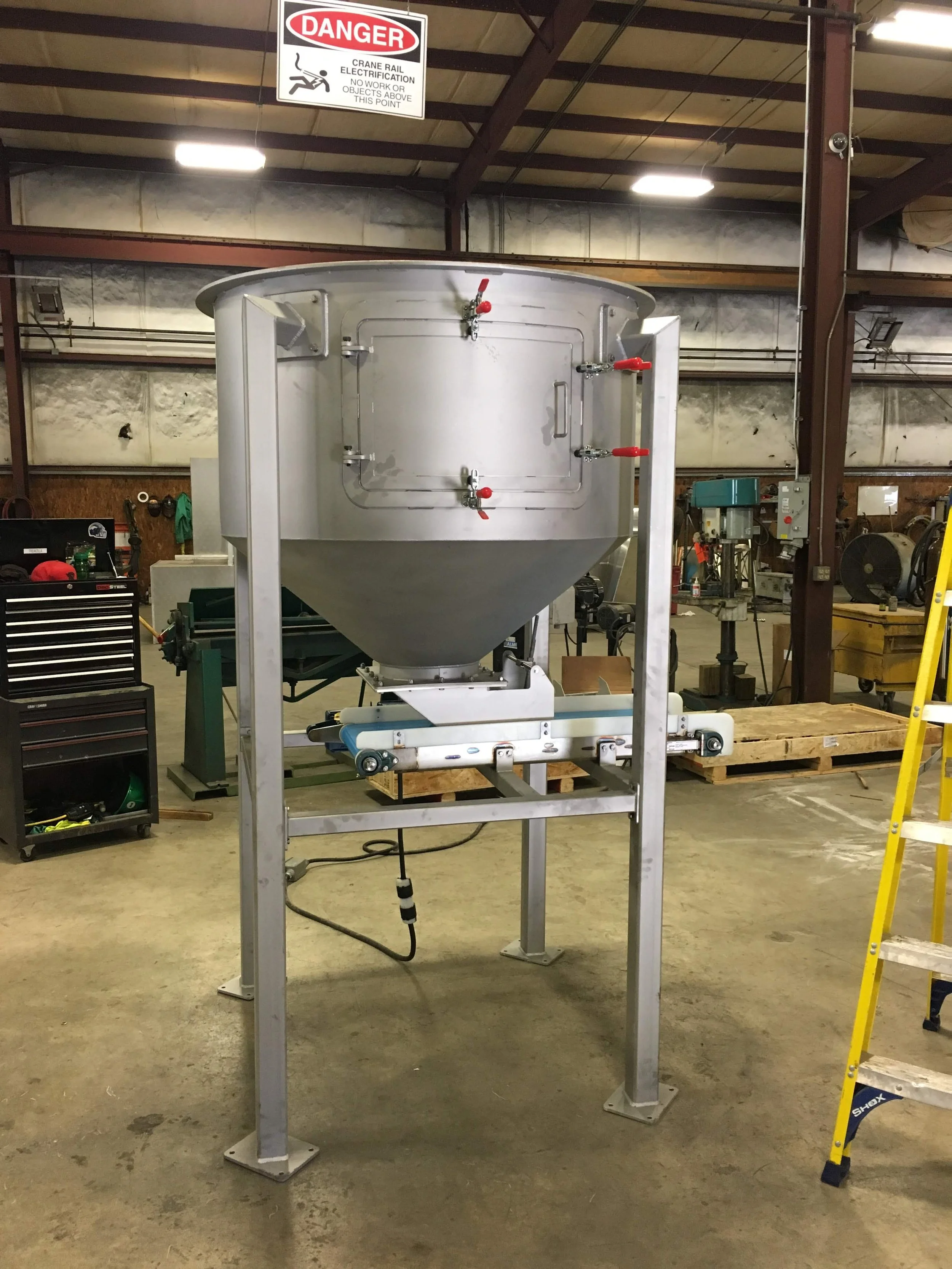 Industrial hopper machine with a warning sign that reads 'Danger' and instructs against work or objects above the crane rail electrical wiring.