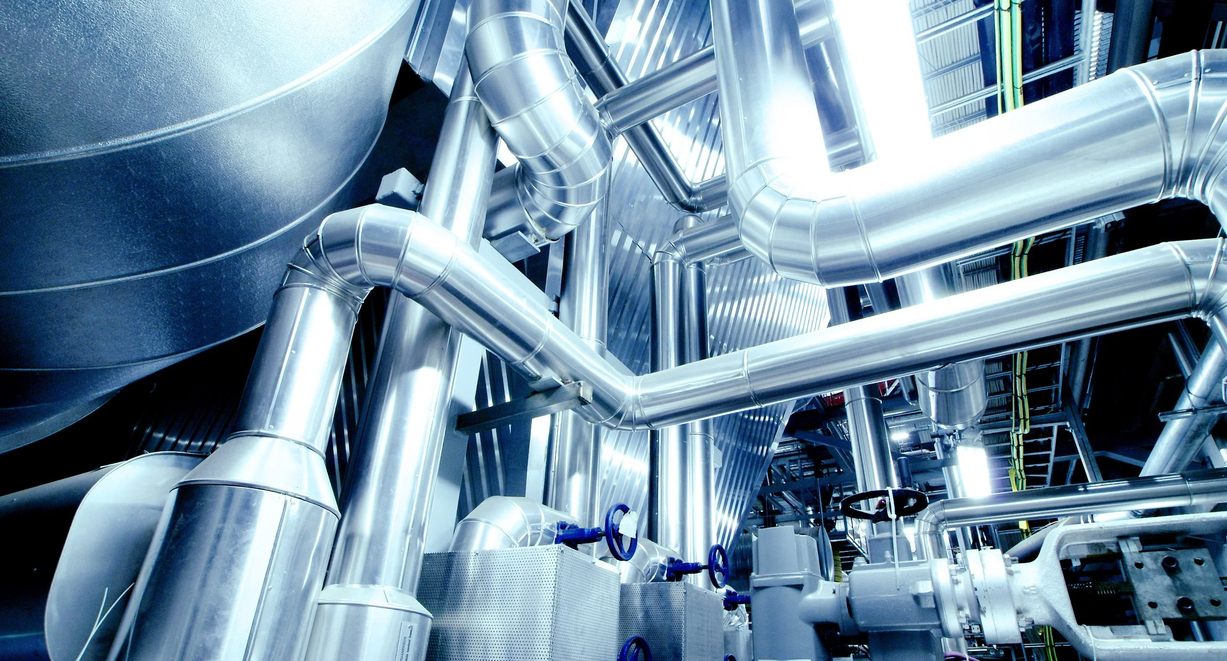 A network of shiny, silver industrial pipes and ducts in a manufacturing or power plant facility.