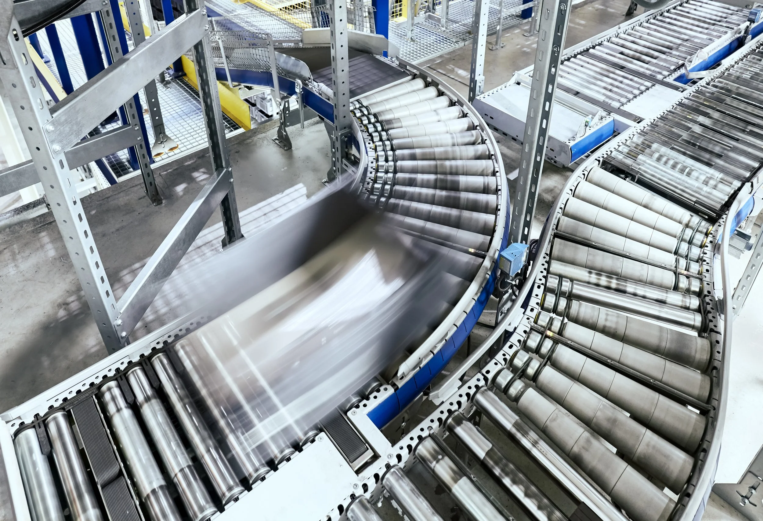 Industrial conveyor system with metal rollers transporting flat object through a manufacturing or packaging facility.