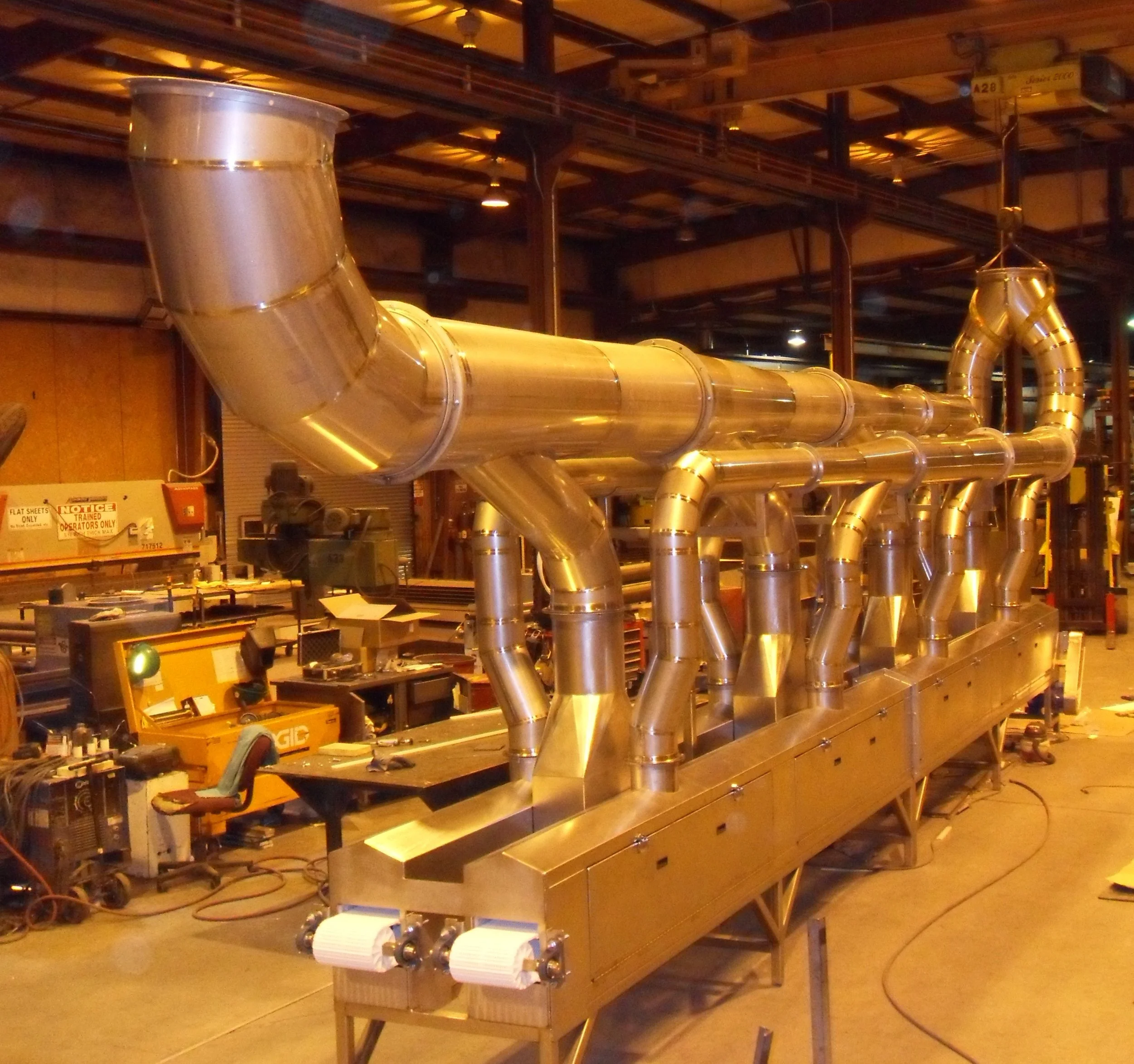 Large industrial stainless steel piping system with multiple bends and connections inside a factory or workshop.