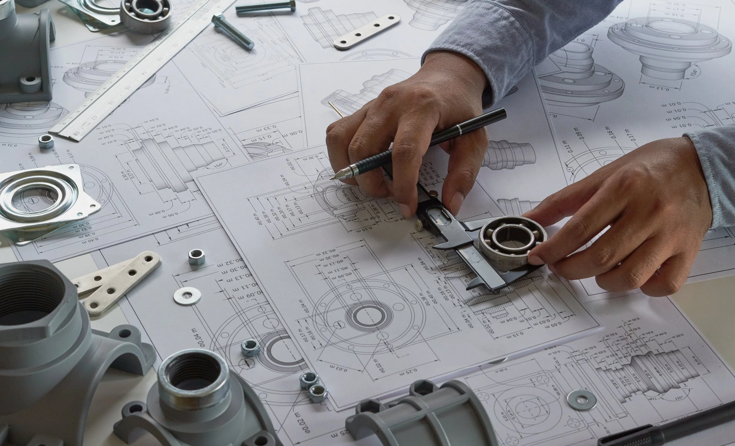 Person working on technical mechanical drawings and parts with caliper and other tools.