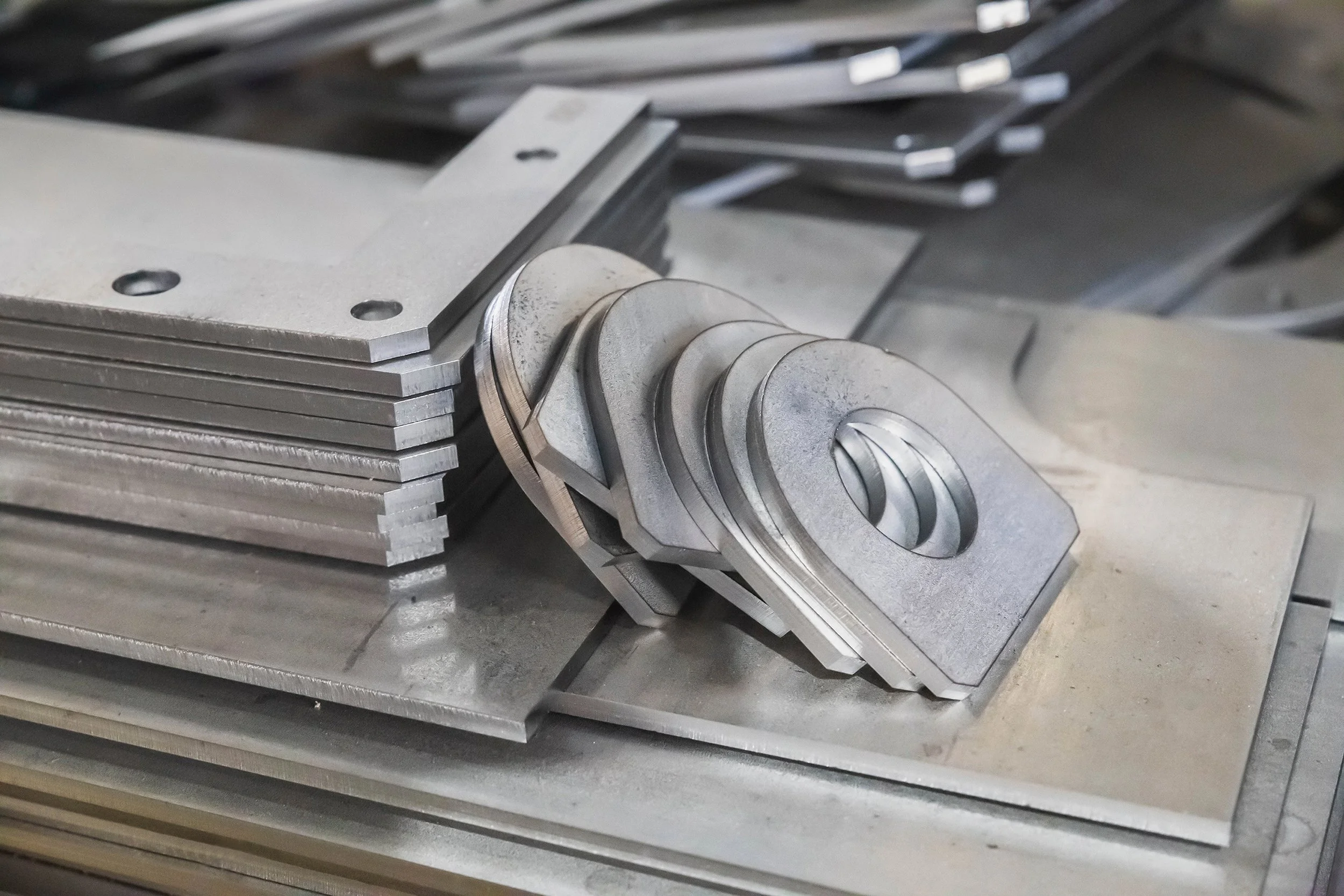 Stacked metal sheets and a set of machined metal parts on a workbench in a factory or workshop.
