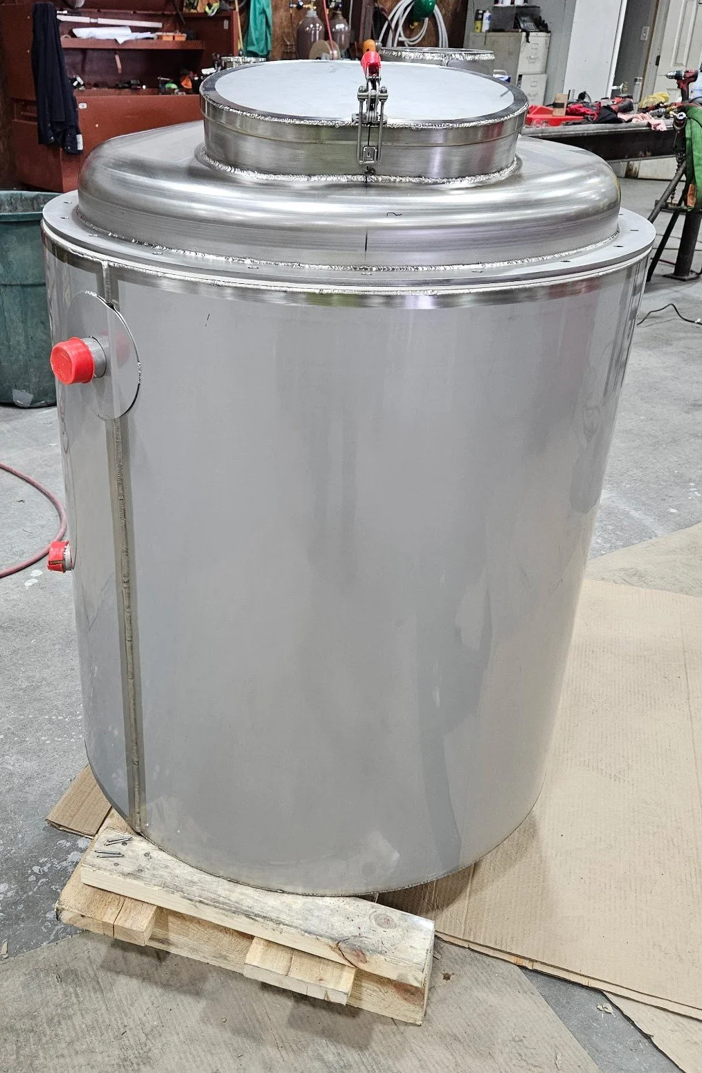 Large stainless steel industrial mixing tank on a wooden pallet in a workshop.