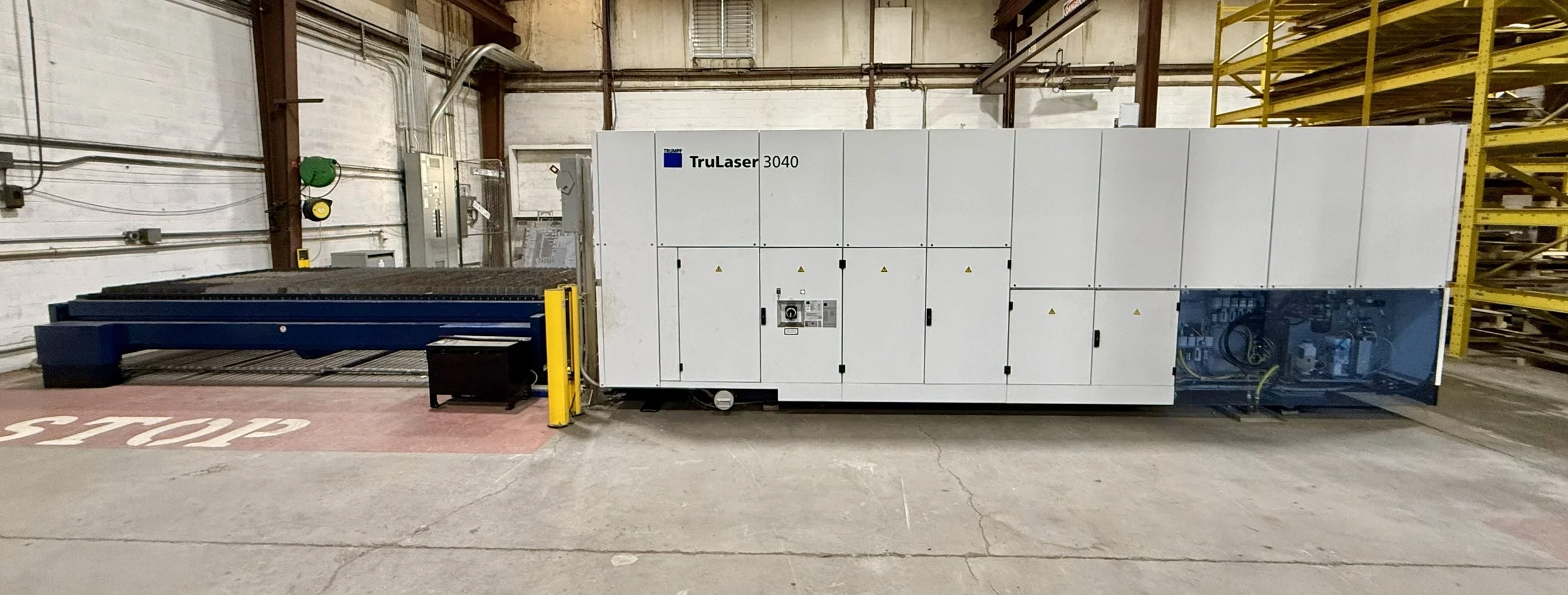 Large industrial laser cutting machine labeled 'TruLaser 3040' inside a warehouse.