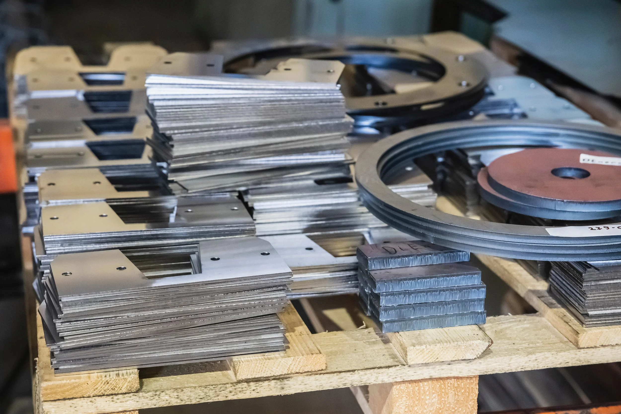 Metal machine parts and circular metal rings stacked on a wooden pallet.