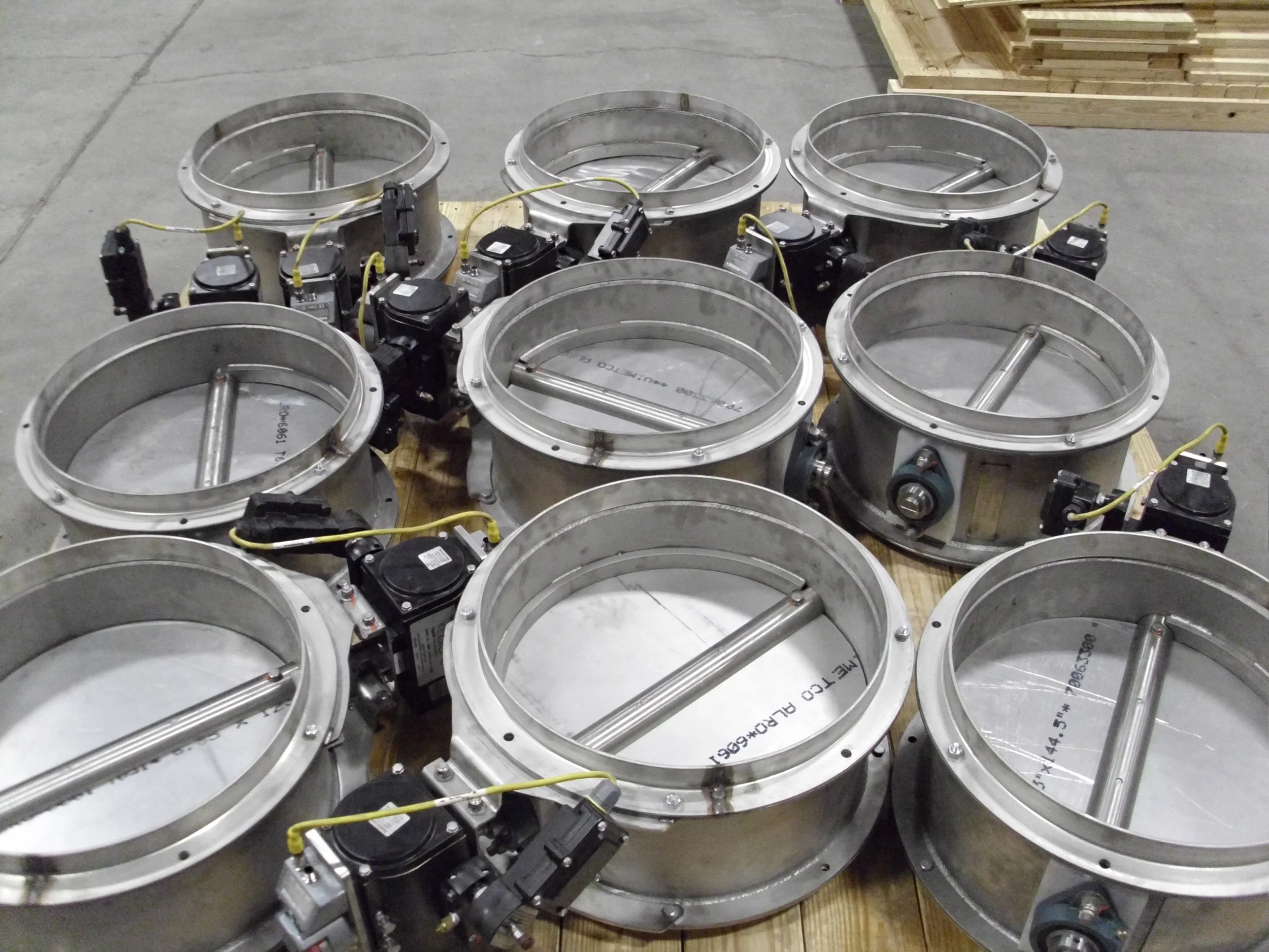 Metal circular industrial components with attached electrical wiring and sensors, placed on a wooden pallet in a warehouse.